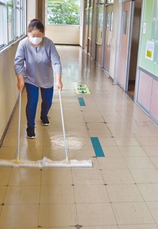 フロア用ワイパーを２本使い、廊下を掃除するＰＴＡ役員。掃除をする中で、２本同時にフロア用ワイパーをかけると効率が良いことに気が付いたという