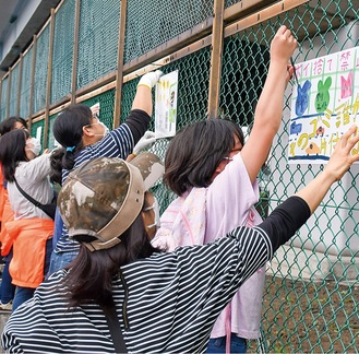 フェンスにポスターを掲示していく児童ら