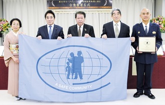 新しいセーフコミュニティのフラッグを手にする（左から）白石代表理事、井上議長、小林市長、宮田会長、盾を手にする押部署長