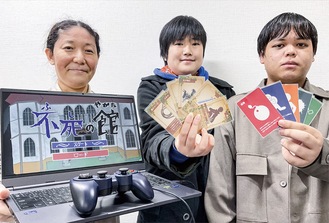 パソコン用ゲーム（左）を持つ高木准教授とカードゲーム開発も手掛けた学生