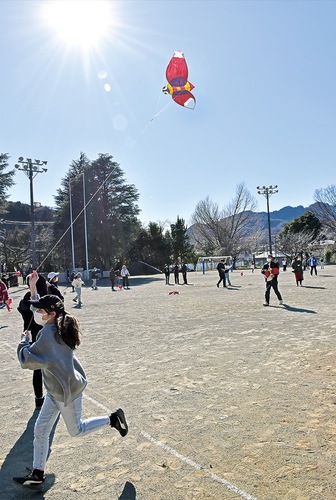 グラウンドを駆け回りながら凧揚げを楽しむ児童ら