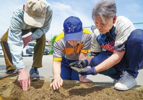 施設職員（右）の差し出したひまわりの種を植える利用者
