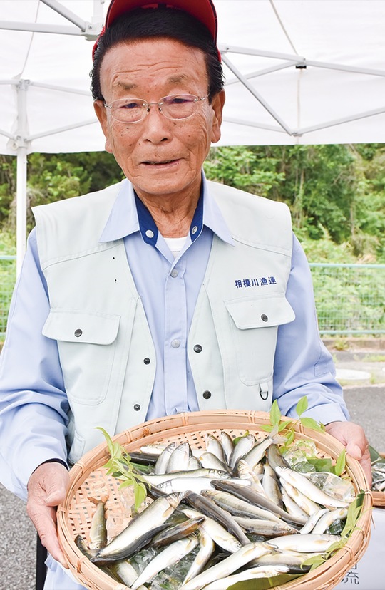 ザルに盛られたアユを見せる木藤会長