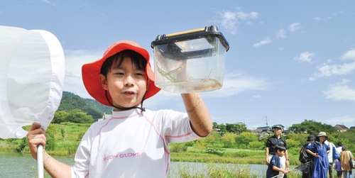 バッタが入った虫かごを嬉しそうにのぞき込む参加者