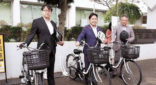 市役所本庁舎のステーションに並んだ自転車と黒田さん（右）と山口市長（中央）、工藤さん