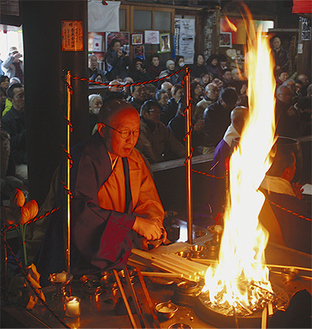 護摩木をくべて炎に照らされる僧侶