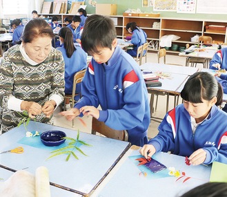 完成した食器に季節の植物を飾り付ける生徒ら。左が講師の村山さん＝12月20日、1年3組の授業で