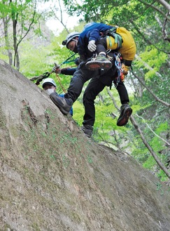 負傷した登山者役の隊員を背負い、高さ７ｍほどの崖の上から降下して搬送する救助隊員