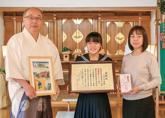 表彰状を持つ大澤さん（中央）と母のミオさん（右）。ポスターのレプリカを持つ目黒宮司