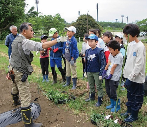 グリーン・インストラクターから野菜の栽培の歴史について学ぶ小学生ら
