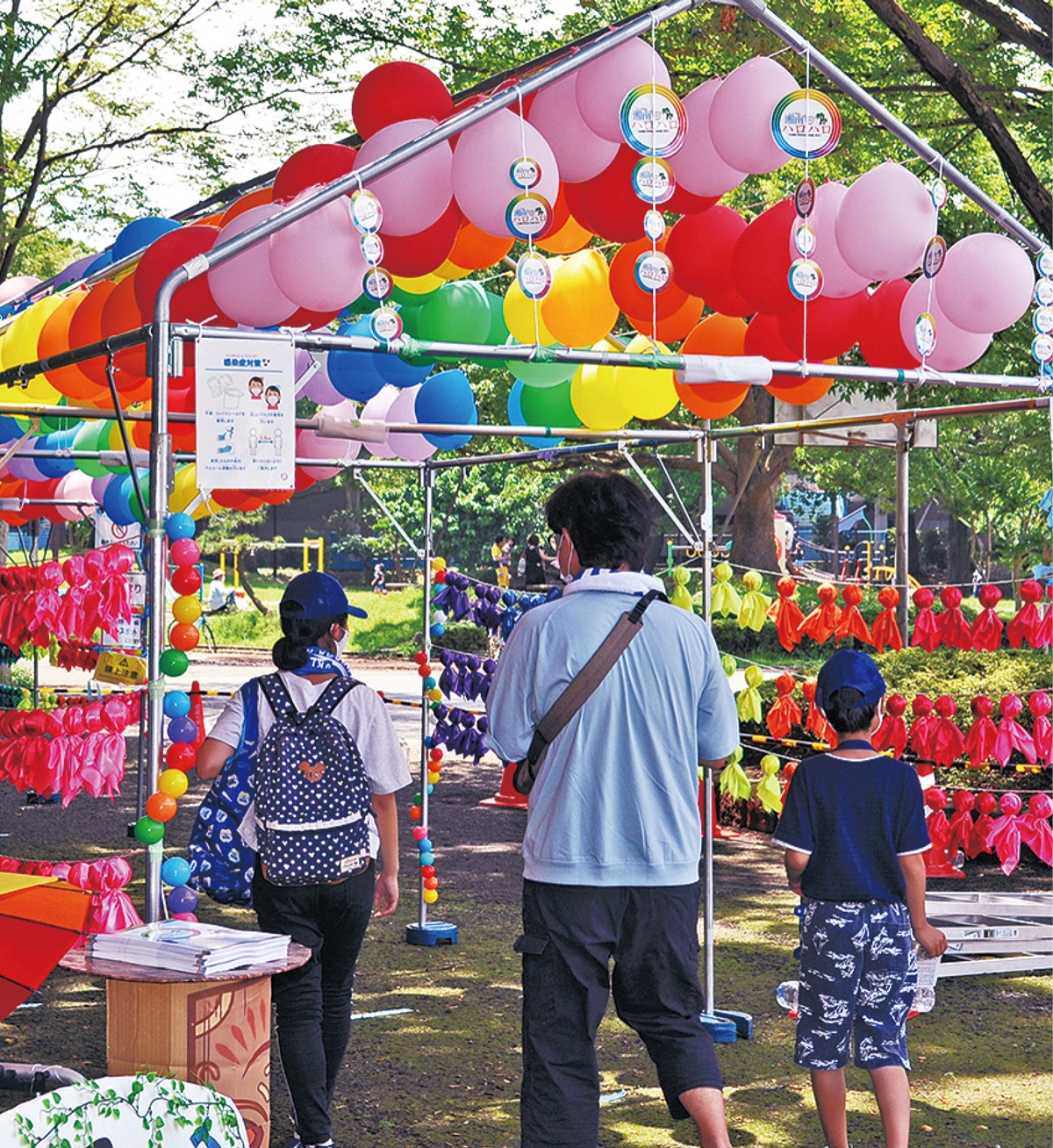 風船などで虹を表したゲートをくぐる家族連れ