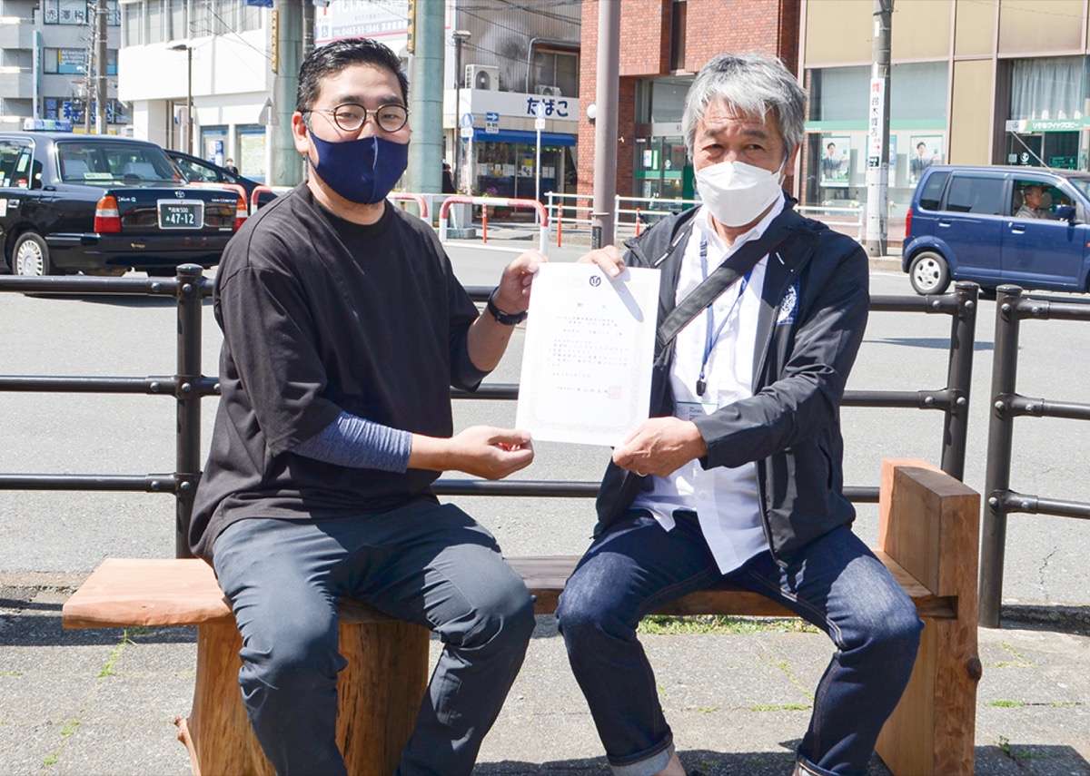 ベンチで感謝状を手にする山口理事長(右)と角田さん