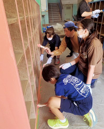 塗装職人の手ほどきでペンキを塗る児童や保護者