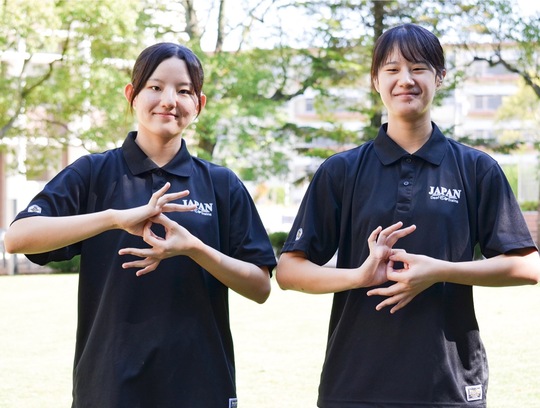デフリンピックを表す手話ポーズをとる志希さん（左）と志野さん