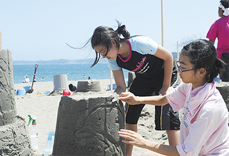 固めた砂を削りイルカの砂像を作る参加者