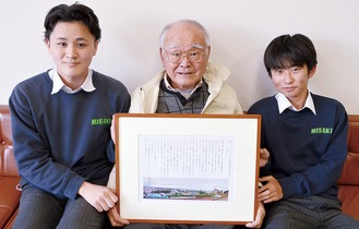 プレゼントした額入りのコラム原稿を手にする高松さん（中央）と池田さん（左）、下里さん（右）
