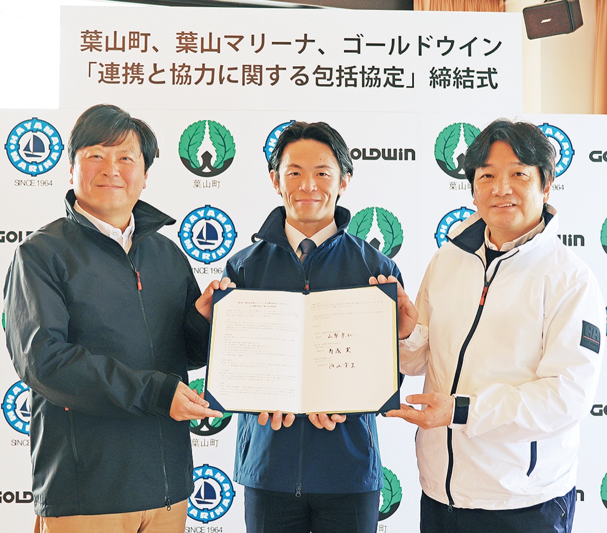 協定書を持つ（左から）葉山マリーナの寿浅社長、山梨町長、ゴールドウインの渡辺社長（提供）