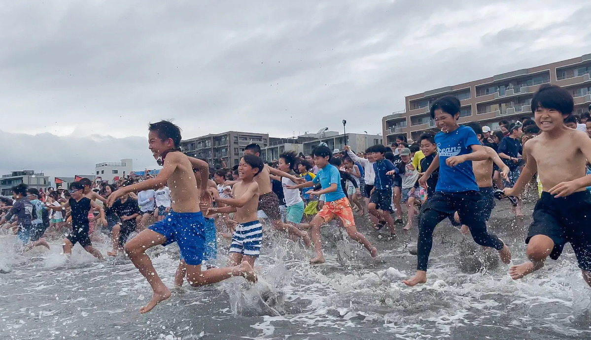 「待ちわびた」と言わんばかりに海岸を駆け、海へ入る児童ら