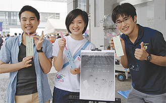 ▲ストーンペーパーで作った短冊を手にする（左から）来場者、仁藤さん、実行委員メンバー