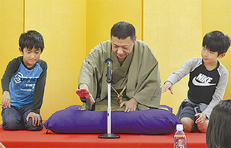 三遊亭圓丸さん（中央）と酒を飲むしぐさを演じる児童