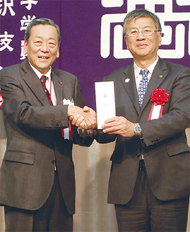 片岡会長（左）から車いすの目録を受け取り握手を交わす鈴木市長