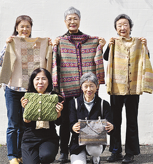 地元の植物を煮出して作ったセーターやカーディガン、バッグを手にメンバーら
