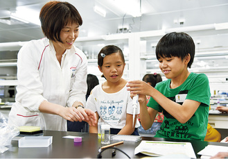 薬づくりの実験を教わる小学生