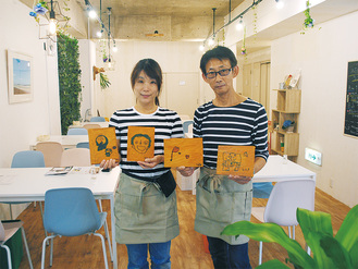 ニコズキッチンを運営する小木曽代表（左）と大塚淳一副代表（左）。手にあるトレーのイラストは近くの小学校の特別支援学級の手による。「多くの方の支援があってこそ」と代表