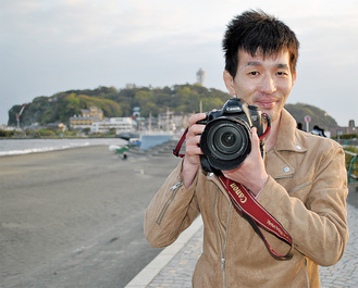 江の島を背景にカメラを構える亀崎さん
