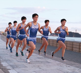 江の島を背景に海沿いを走る同部の選手ら（写真は提供）