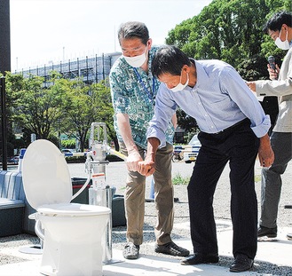 井戸水による水洗を試す佐藤市長（左）と、綾社長