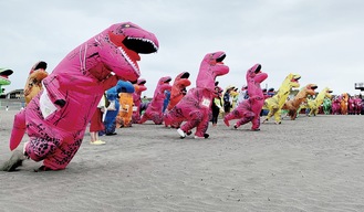 恐竜の着ぐるみ姿で砂浜を全力疾走する参加者（＝6日、鵠沼海岸）