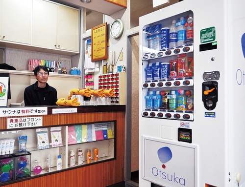 午後３時の開店とともに、カウンターで常連客を待つ「富士見湯」３代目店主の白石重治さん（50）。タオルや洗面用具なども随時販売している。その前には「銭湯の定番」とも言われる大塚製薬（株）の自動販売機も稼働。存在感を放っている。なかには「ポカリ」がたくさん