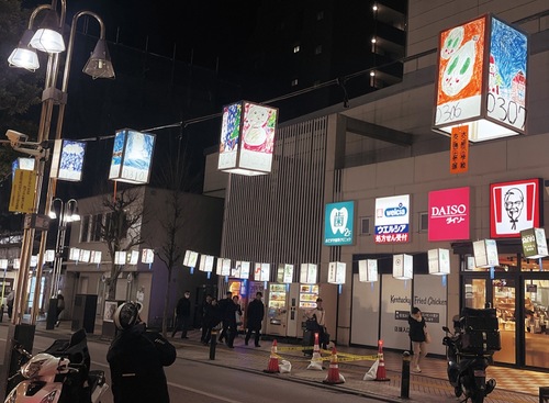 児童の絵が貼られたあんどんを見上げる通行人