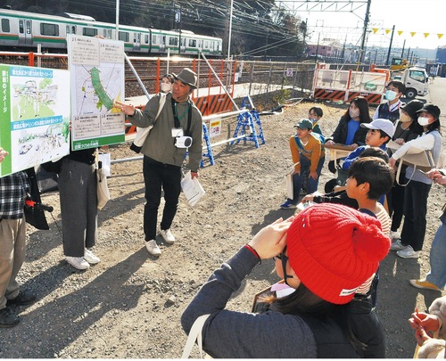工事が進む新駅予定地でまちづくりについて説明する中島さん（左）とそれを聞く参加者