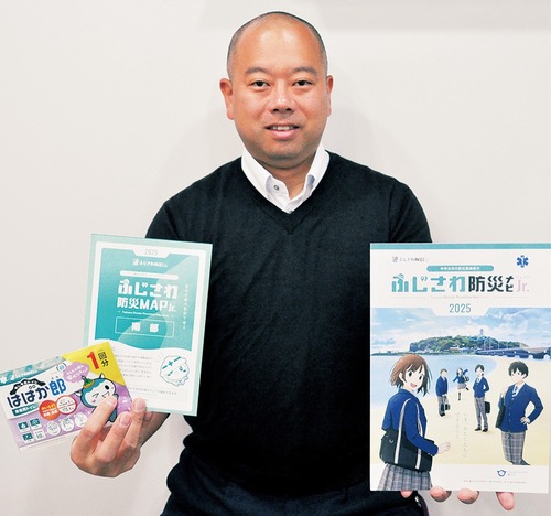 完成したばかりの防災冊子と防災ハザードマップ、非常用トイレを手にする櫻井さん