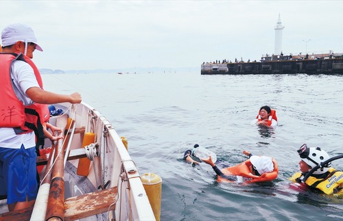 ボートから投げ入れられたひも付きのペットボトルをつかんで救助される団員ら