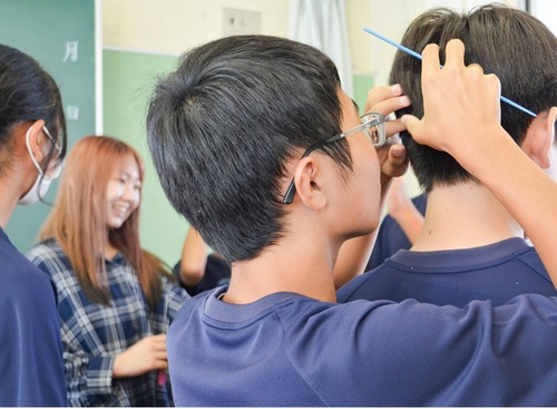 美容師の櫛で同級生の髪をとかす生徒
