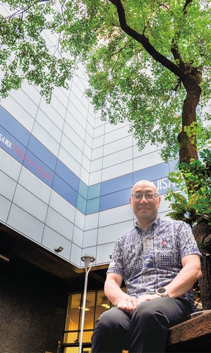 ビル３棟の中庭に位置するハゼの木広場に腰かける山田さん