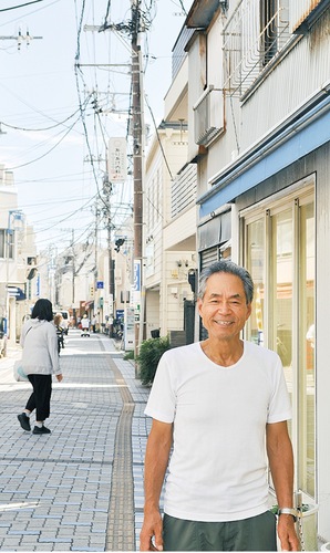人が行き交う石畳の上で笑顔を見せる飯田理事長