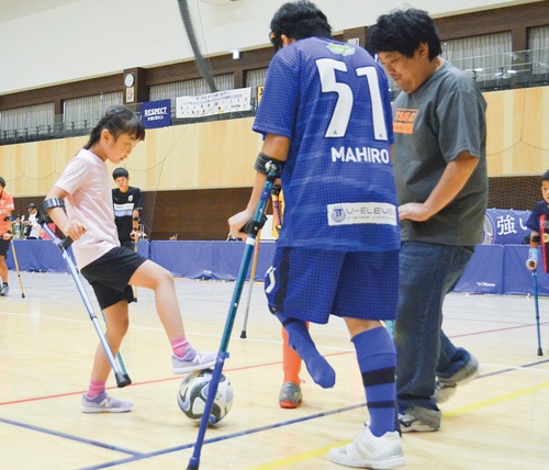 クラッチという杖を使用してアンプティサッカーをプレーする児童
