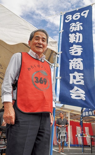 「３６９」と書かれた旗の横で秋まつりの来場者を迎え入れる渡部さん