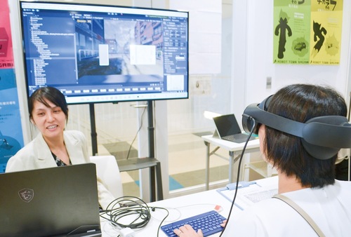 避難体験をしている女性（右）と女性が見ている仮想空間（中央）