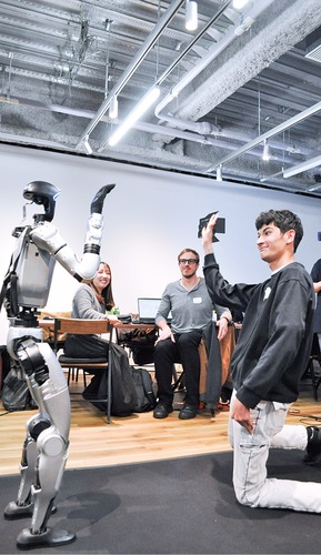 手を振るロボット（左）とミロさん（右）、それを見守るチームメンバーたち（中央）
