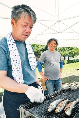 額に汗を流しながら「能登いわし」を網で焼く芳賀代表（左）とそれを見守る栗原実行委員長