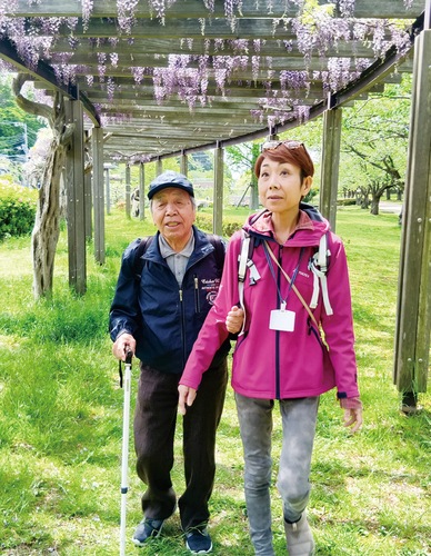 藤の花咲く下を歩く宮崎さん（左）