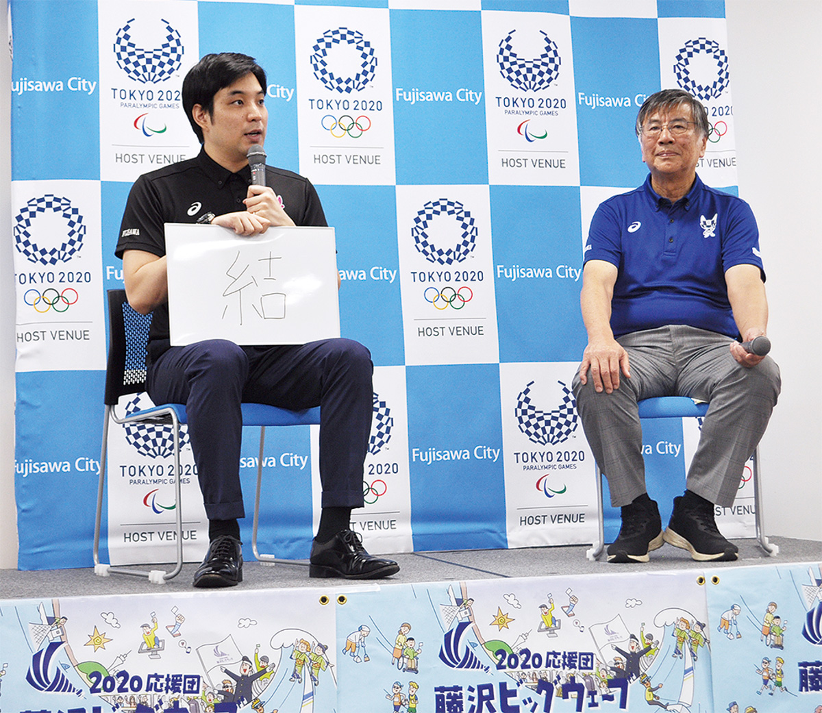 市役所で開かれた公開記者会見で五輪開催の抱負を「結」と紹介する元競泳選手の立石諒さん（左）