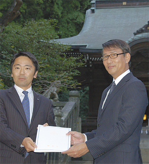 クールながらも、ユーモアたっぷりの中井さん（右）。松尾市長から委嘱状を受け取った＝24日市内坂ノ下