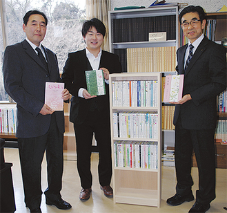 詩集を収めた本棚と（右から）安良岡教育長と西野さん、立川さん