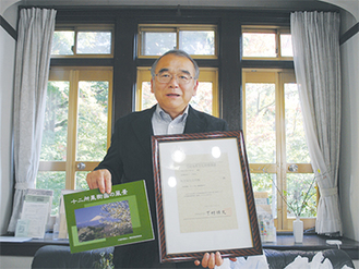 旧坂井邸の登録有形文化財登録証と、４月に刊行した写真集を手にする兵藤理事長